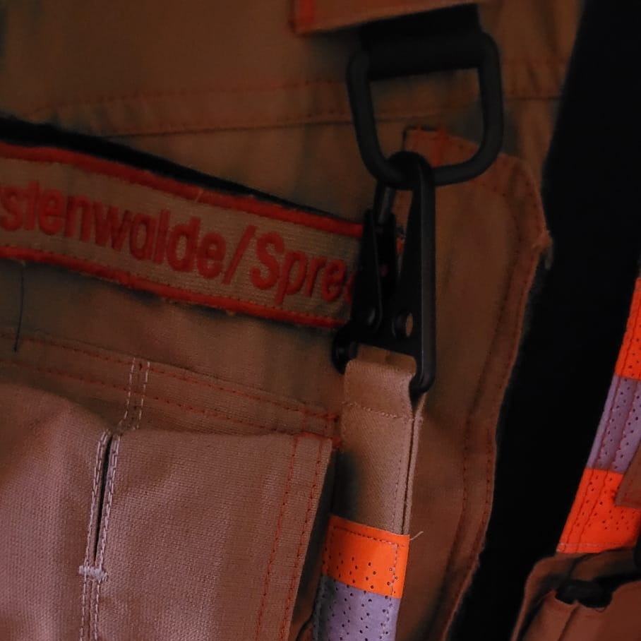 "Schwarzer Taktik-Karabiner des Feuerwehr-Handschuhhalters eingehängt an Einsatzjacke der Feuerwehr Fürstenwalde/Spree – Detailansicht der schnellen Befestigung an der PSA"