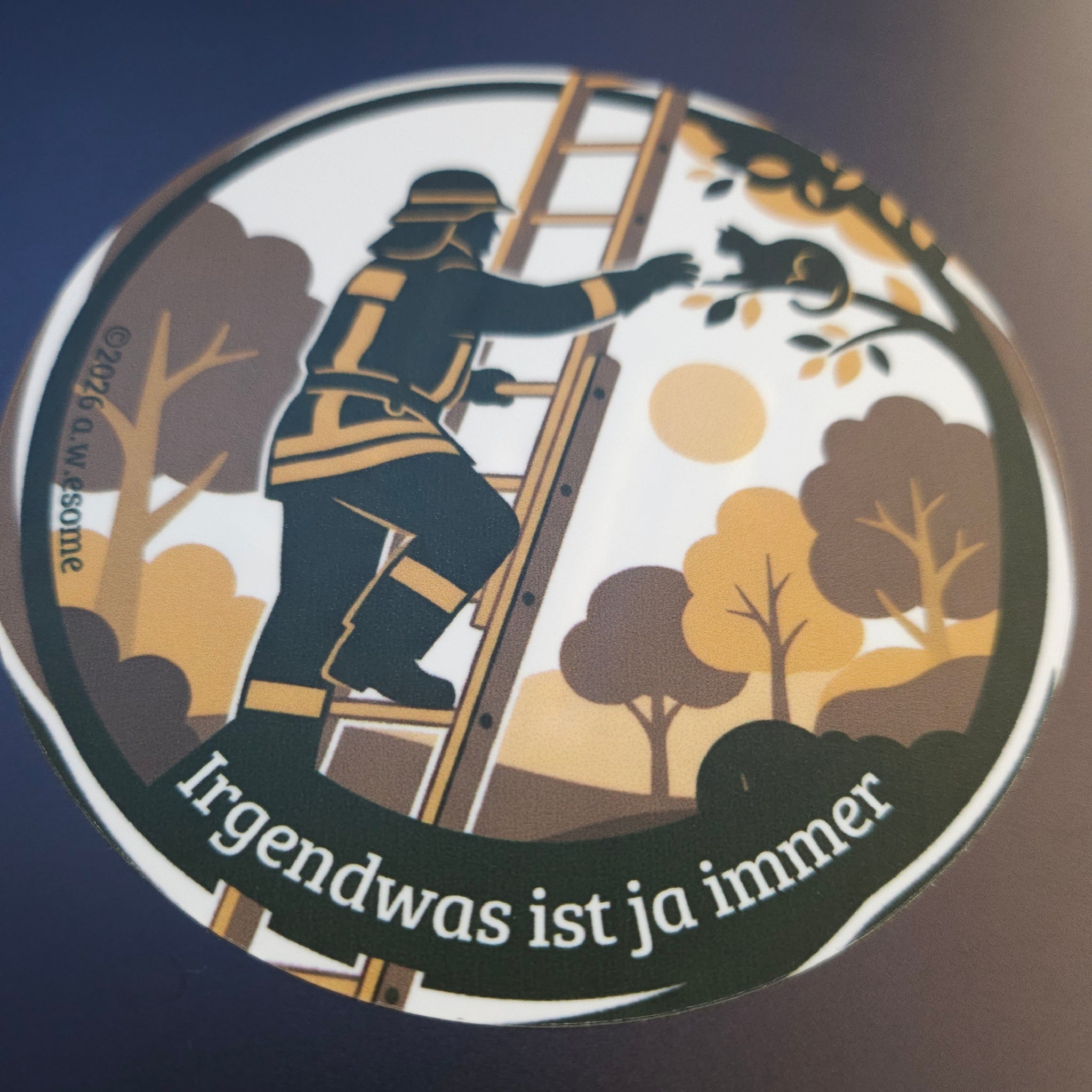 Runder Feuerwehr-Sticker aufgeklebt auf einer dunklen Oberfläche im kontrastreichen Wachen-Design.
