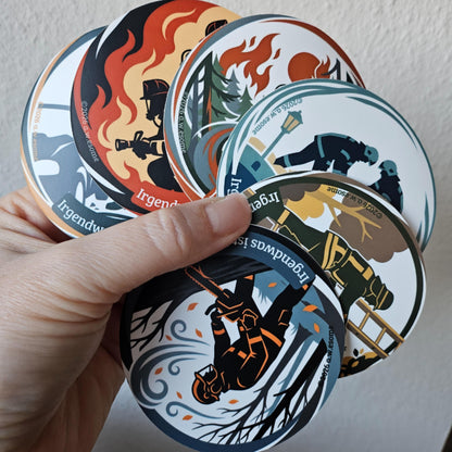 Eine Hand hält gefächerte, runde Feuerwehr-Sticker der Einsatzserie mit dem Slogan Irgendwas ist ja immer.