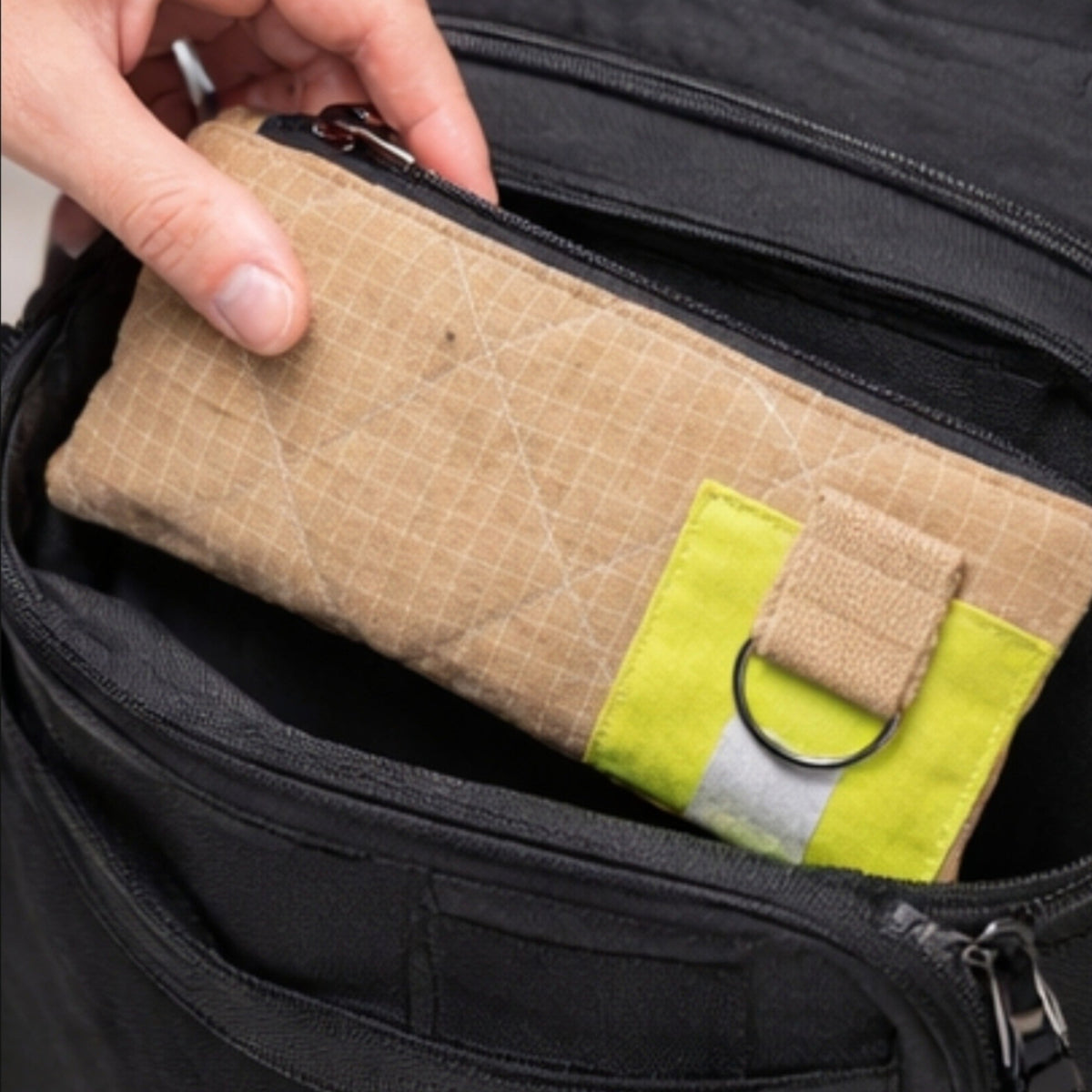 Ein beiges UNIT 112 Gear-Bag aus Upcycling-Material wird in das Hauptfach eines schwarzen Rucksacks gesteckt.