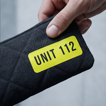 Eine Hand hält das flache, schwarze Mäppchen mit reflektierendem UNIT 112 Patch vor einem hellen Hintergrund