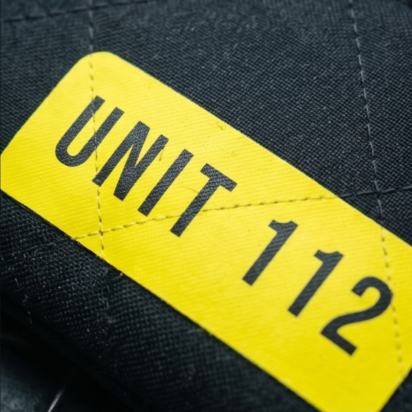 Detailansicht des neongelben, reflektierenden Klettverschluss-Patches mit schwarzer Aufschrift UNIT 112 auf dunklem Stoff.