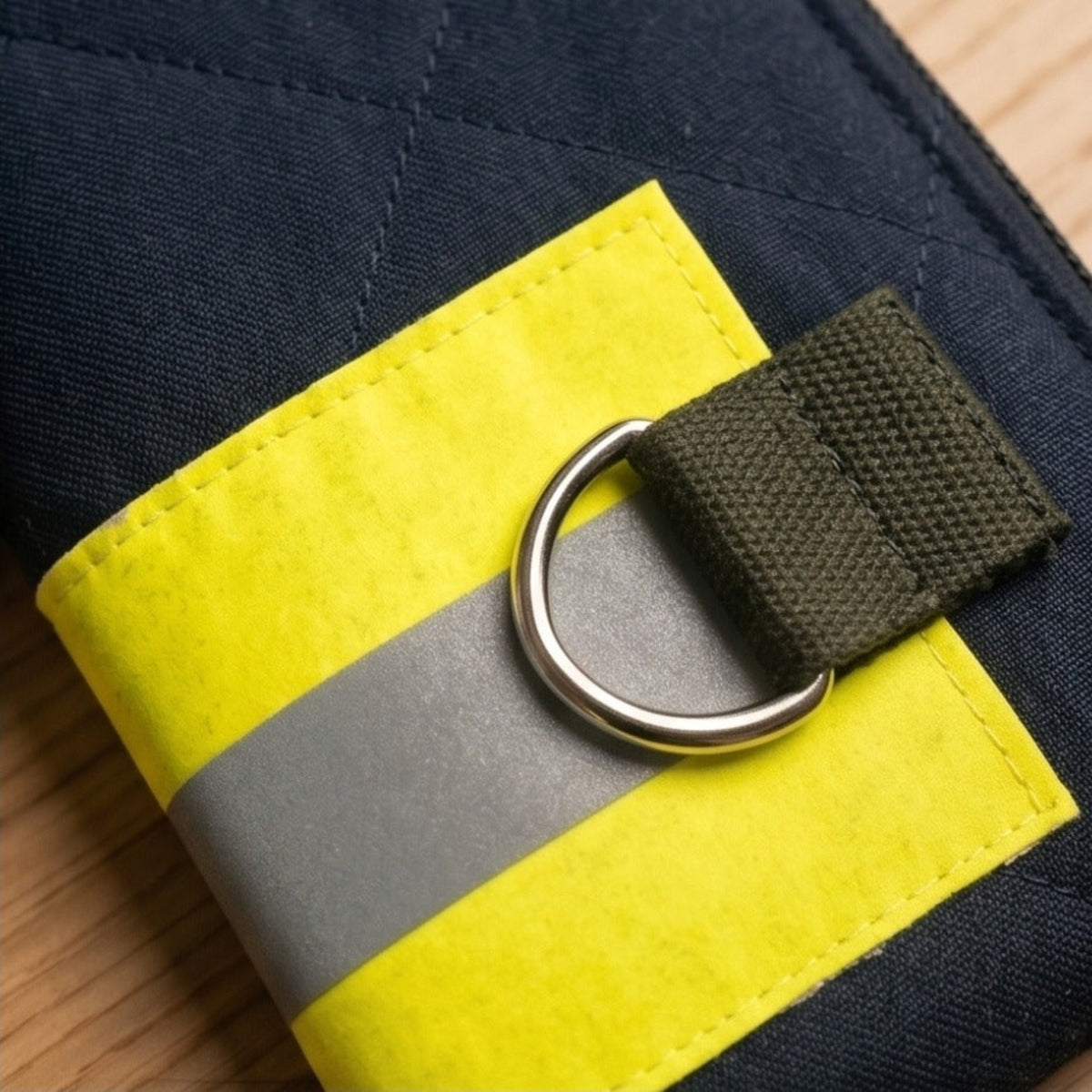 Makroaufnahme des gelben Feuerwehrschlauch-Details mit einem silbernen D-Ring aus Metall an der Außenseite der Tasche.