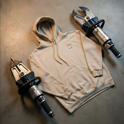 Sandfarbener Kapuzenpullover flach liegend auf Werkstattboden, umgeben von schwerem hydraulischen THL-Rettungsgerät der Feuerwehr.
