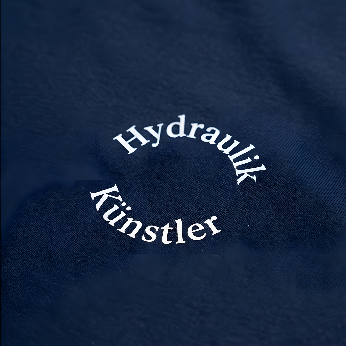 Detailansicht des runden, weißen Brust-Aufdrucks Hydraulik Künstler im minimalistischen Bogen-Design auf dunkelblauem Stoff.