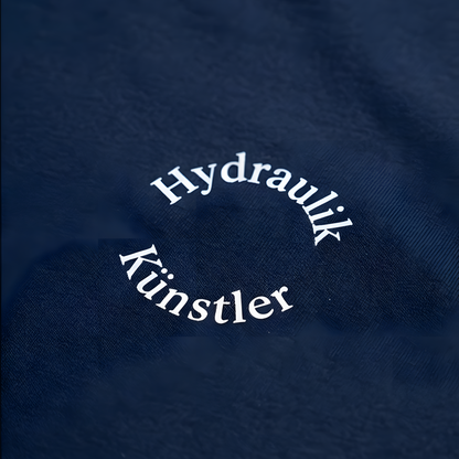 Detailansicht des runden, weißen Brust-Aufdrucks Hydraulik Künstler im minimalistischen Bogen-Design auf dunkelblauem Stoff.