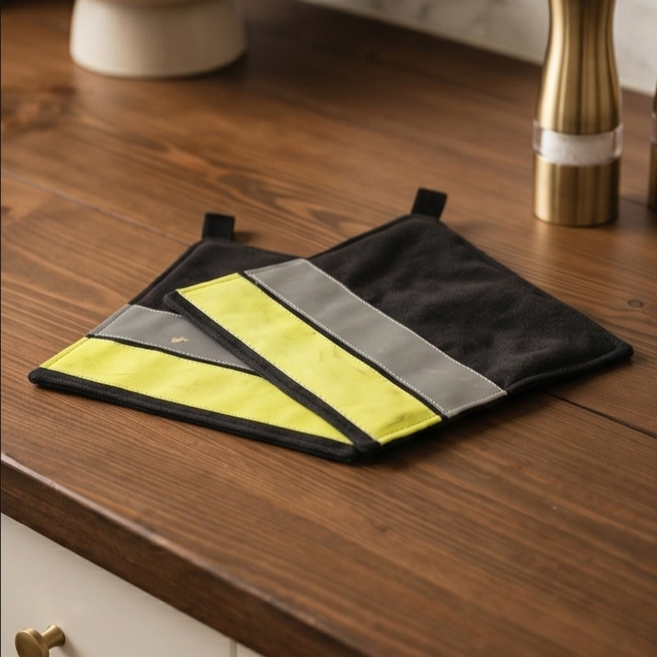 Ein Set aus zwei robusten Upcycling-Feuerwehr-Topflappen liegt dekorativ auf einer hölzernen Küchenarbeitsplatte neben einer Pfeffermühle.
