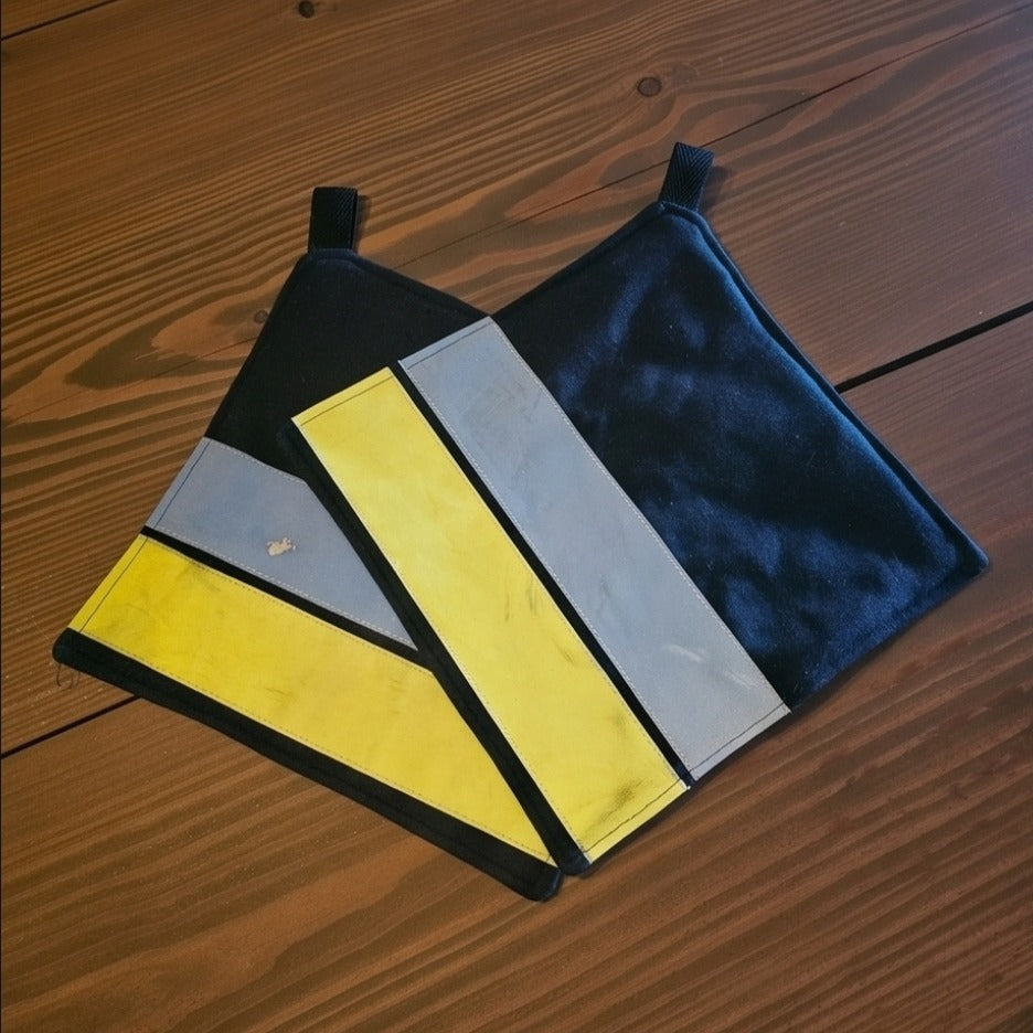 Draufsicht auf die zwei quadratischen Feuerwehr-Topflappen aus hitzebeständigem Aramid-Stoff mit leuchtenden Warnstreifen.
