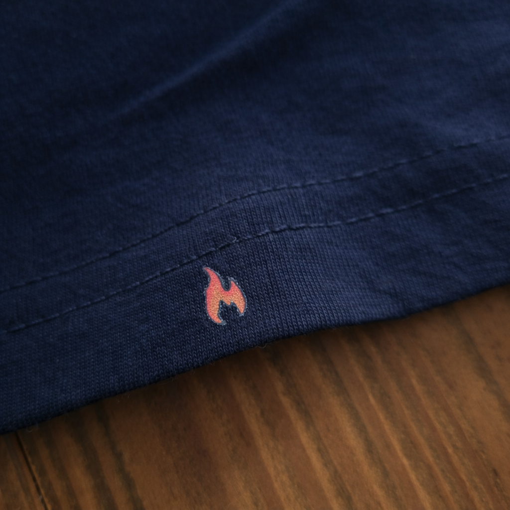 Nahaufnahme einer kleinen roten Flamme, die auf den Saum des navy-blauen Feuerwehr-THL-Shirts gedruckt ist.