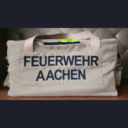 Upcycling-Feuerwehrtasche aus beiger Feuerwehrjacke mit dunkelblauem Aufdruck FEUERWEHR AACHEN und hellen Tragegurten.