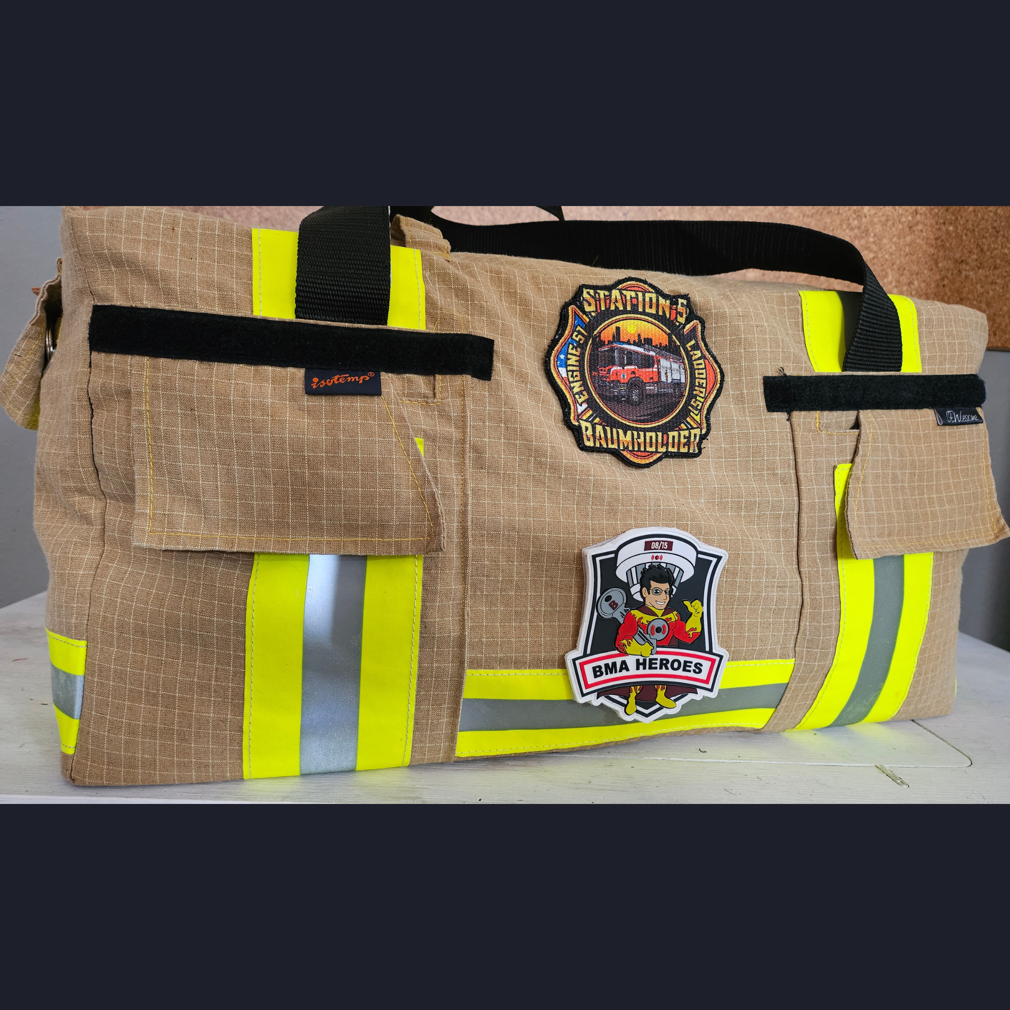 Upcycling-Feuerwehrtasche aus beiger Einsatzkleidung mit gelb-silbernen Reflektoren sowie Station 5 Baumholder und BMA Heroes Patches.