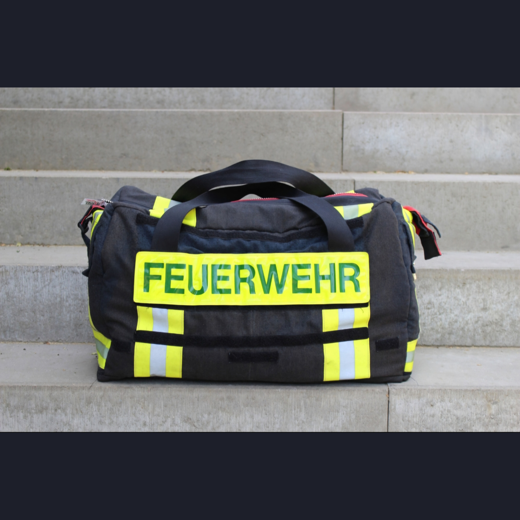 Personalisierte Upcycling-Feuerwehrtasche aus schwarzer Feuerwehrjacke mit gelb-silbernen Reflektorstreifen und FEUERWEHR-Klettschild.