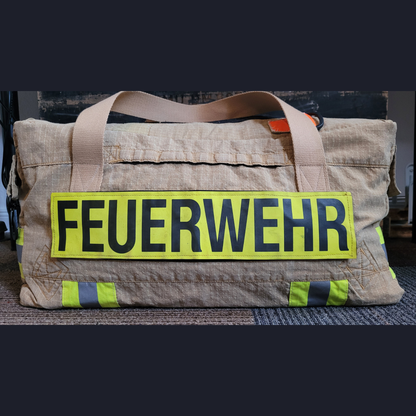 Personalisierte Upcycling-Feuerwehrtasche aus beiger Einsatzkleidung mit Tragegurten und großem gelben FEUERWEHR-Klettschild.