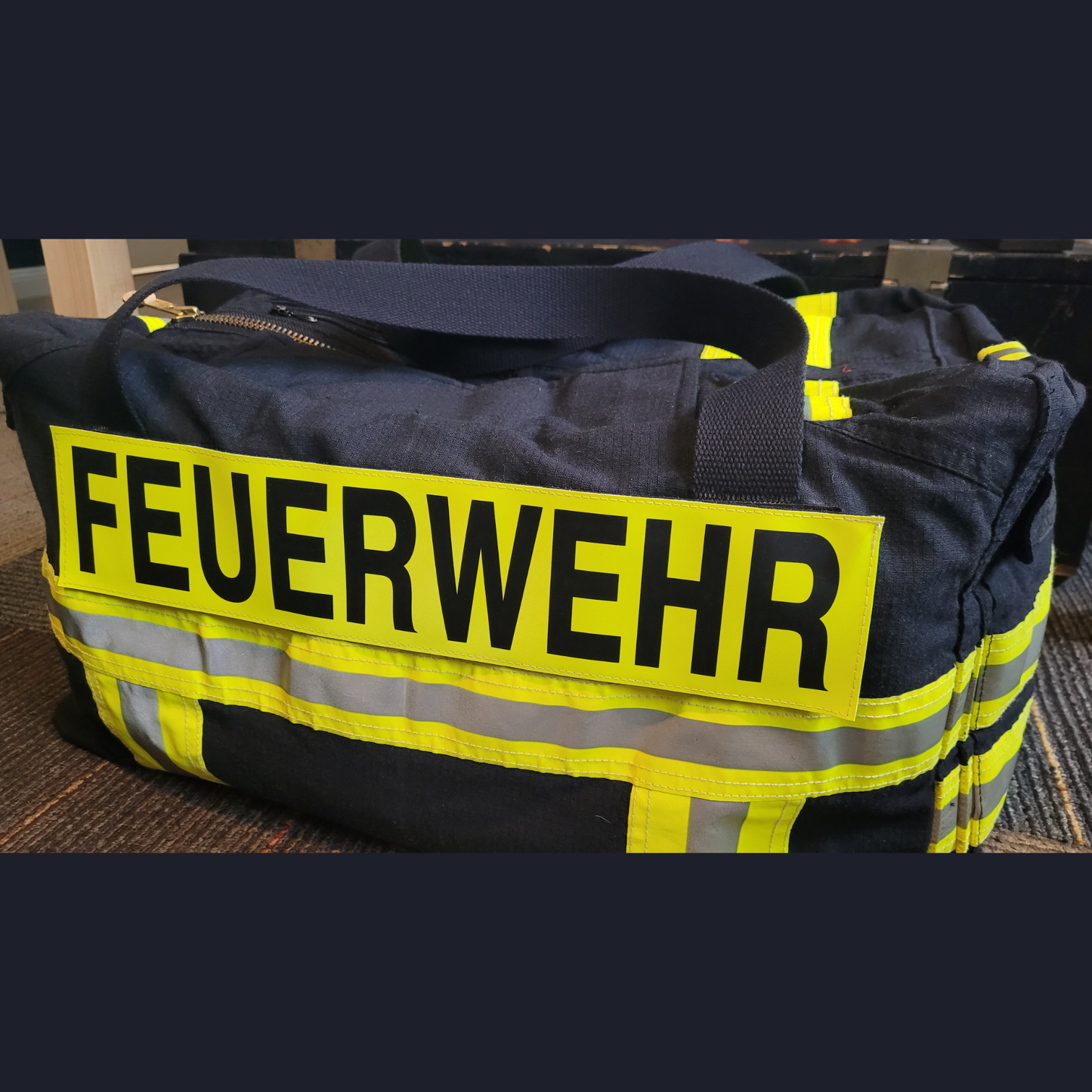 Personalisierte Upcycling-Feuerwehrtasche aus schwarzer Feuerwehrjacke mit gelb-silbernen Reflektorstreifen und FEUERWEHR-Klettschild.