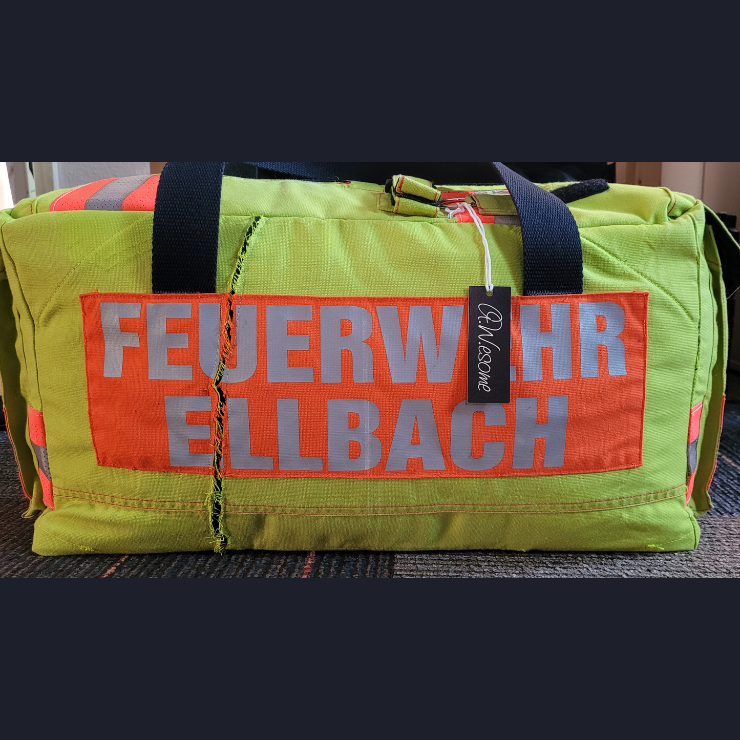 Upcycling-Feuerwehrtasche aus neongelber Jacke mit orangefarbenem Rückenaufdruck FEUERWEHR ELLBACH und A.W.esome-Markenanhänger.