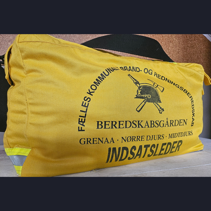 Upcycling-Feuerwehrtasche aus gelber Einsatzkleidung mit dänischem BEREDSKABSGÅRDEN INDSATSLEDER Rückenaufdruck und Helm-Logo.