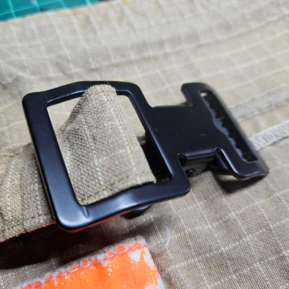 "Detailansicht: Schwarze Metallschnalle und Taktik-Clip aus Zinklegierung am sandfarbenen Aramid-Gurtband des Feuerwehr-Handschuhhalters mit orangenem Reflexstreifen"