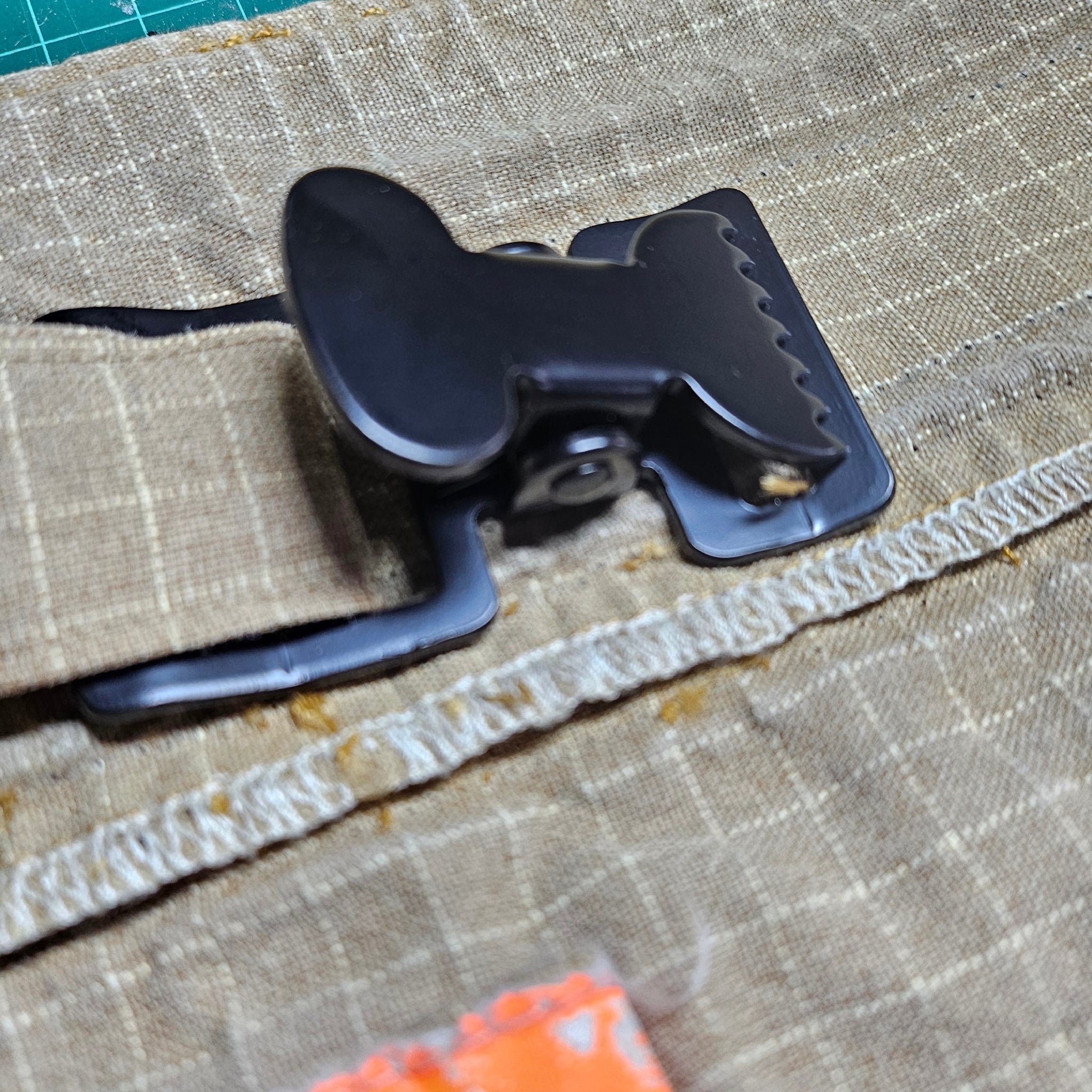 "Rückansicht des schwarzen Taktik-Clips aus Zinklegierung auf sandfarbenem Feuerwehr-Aramidstoff – robuste Verarbeitung des Handschuhhalters für die Technische Hilfeleistung"