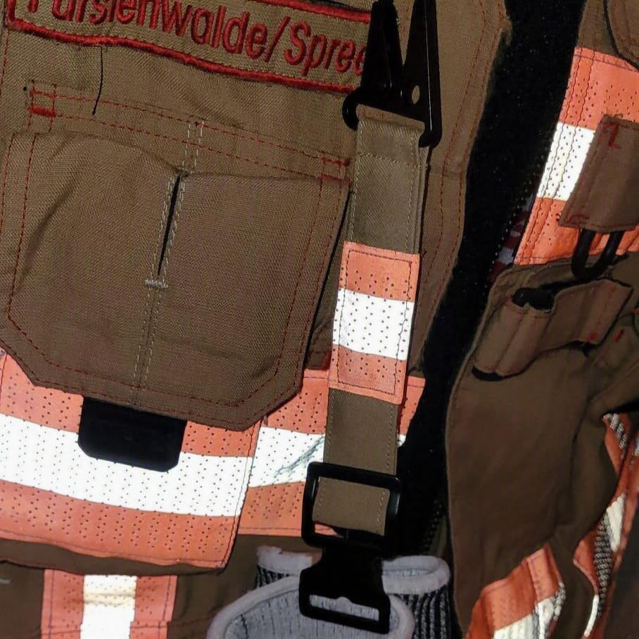 "Feuerwehr-Handschuhhalter mit Taktik-Karabiner an echter Einsatzjacke der Feuerwehr Fürstenwalde/Spree – sandfarbener Aramidstoff mit orangenem Reflexstreifen im Einsatz"