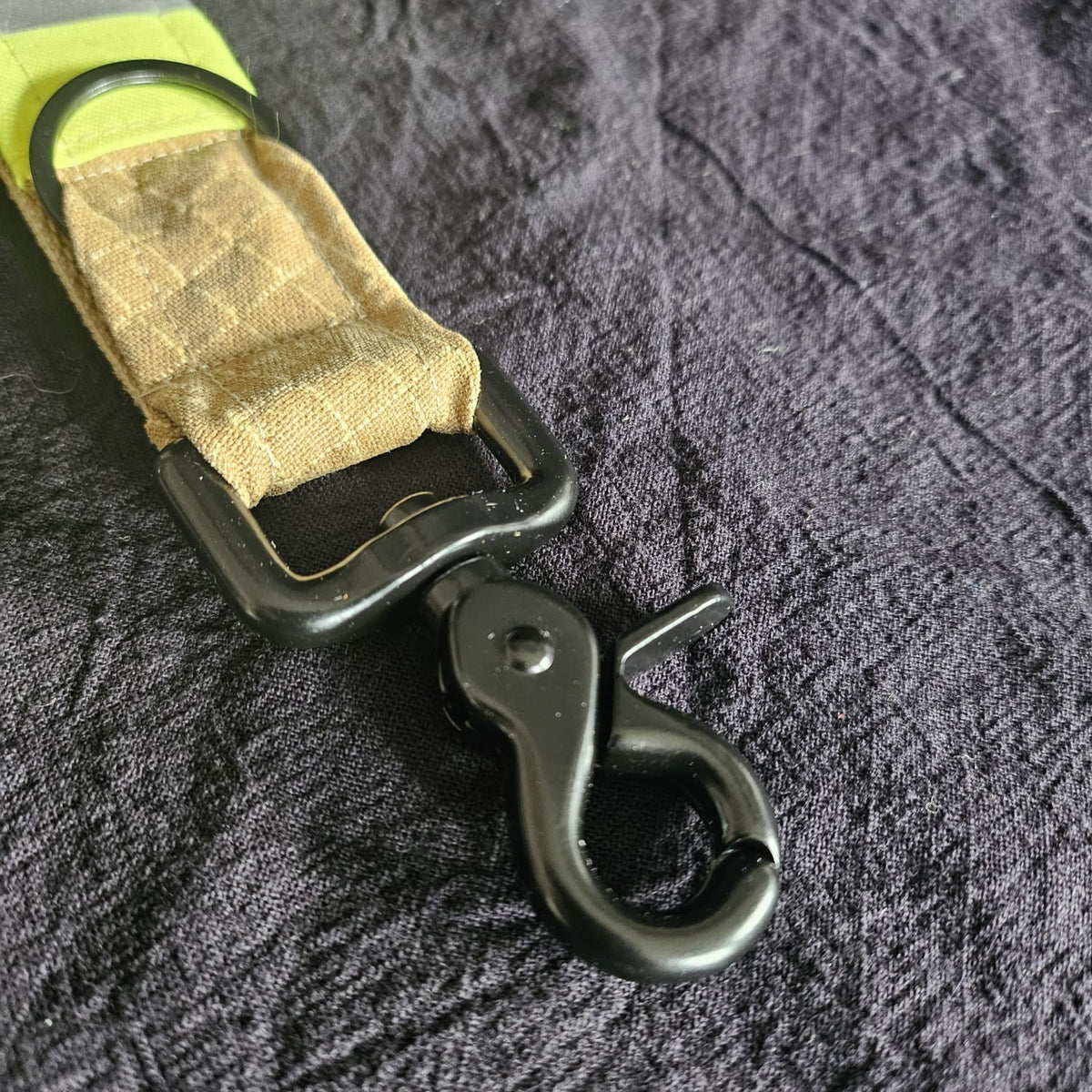 "Schwarzer Scherenkarabiner und Schlüsselring am sandfarbenen Feuerwehr-Handschuhhalter aus Aramid-Einsatzstoff mit neongelben Reflexstreifen – Detailansicht der Befestigungsmechanik"

