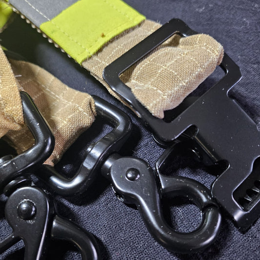 "Nahaufnahme: Schwarzer Scherenkarabiner und Metallschnalle am sandfarbenen Feuerwehr-Handschuhhalter mit neongelben Reflexstreifen aus Aramid-Einsatzstoff"