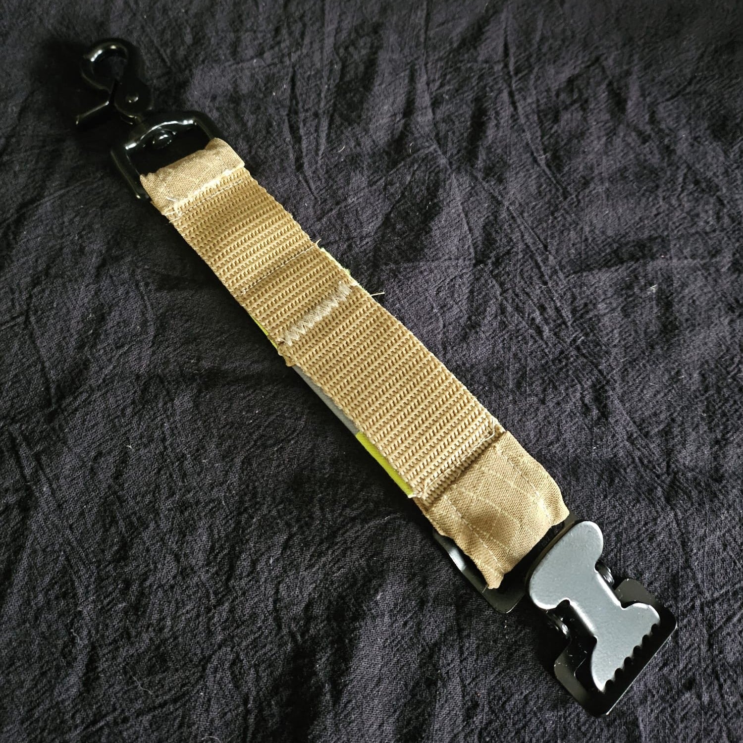 "Rückseite des Feuerwehr-Handschuhhalters aus sandfarbenem Aramid-Gurtband mit schwarzem Scherenkarabiner und Metallschnalle – handgenähtes Upcycling-Accessoire für die Technische Hilfeleistung"