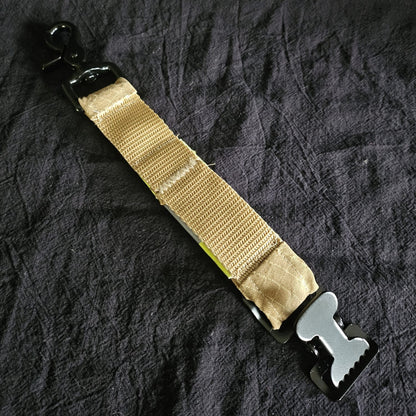 "Rückseite des Feuerwehr-Handschuhhalters aus sandfarbenem Aramid-Gurtband mit schwarzem Scherenkarabiner und Metallschnalle – handgenähtes Upcycling-Accessoire für die Technische Hilfeleistung"