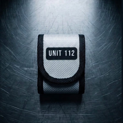 "Upcycling Meldertasche für Swissphone s.QUAD aus weißem Feuerwehrschlauch mit schwarzem UNIT 112 Print und schwarzer Gurtband-Einfassung – Frontansicht auf Metalluntergrund"