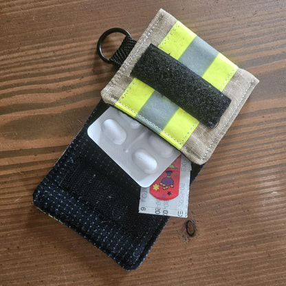 "Geöffnete Feuerwehr Mini-Notfall-Tasche sandfarben mit Medikamenten-Blister und Pflastern – als kompakte Reiseapotheke, D-Ring und Schlüsselring oben sichtbar"

