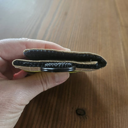 "Feuerwehr Mini-Notfall-Tasche sandfarben – Seitenansicht in der Hand, flache Bauweise ca. 1,5 cm, schwarzer Klettverschluss und D-Ring sichtbar"

