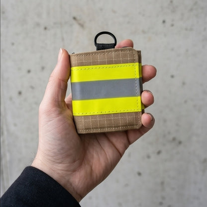 "Feuerwehr Mini-Notfall-Tasche sandfarben kariert mit gelbem Reflexstreifen – in einer Hand gehalten, kompakte Größe ca. 8x8 cm"

