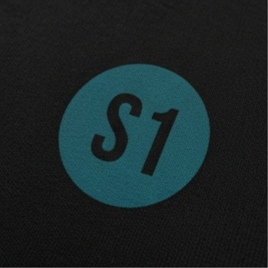 Detailansicht des runden, blau-grünen Brust-Aufdrucks mit dem Schriftzug S1 im minimalistischen Feuerwehr-Funkstatus-Design.
