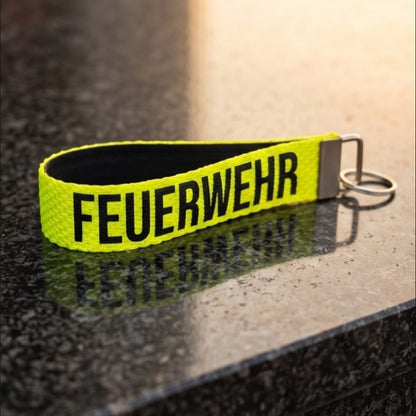 "Neongelber Feuerwehr-Schlüsselanhänger aus robustem Feuerwehrschlauch mit schwarzem FEUERWEHR-Schriftzug und silbernem Schlüsselring – Freisteller"