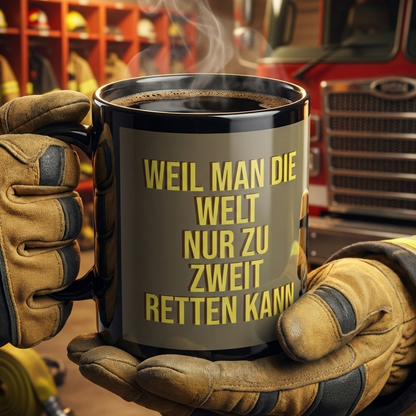 Eine schwarze Tasse aus Keramik. Glänzendes Finish. Abgebildet sind zwei Feuerwehrmänner unter Atemschutz. Text: Weil man die Welt nur zu zweit retten kann.
