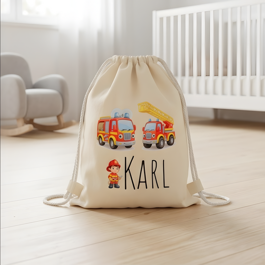 Personalisierter Feuerwehr Turnbeutel aus heller Baumwolle mit dem Namen Karl und zwei bunten Comic-Feuerwehrautos in einem hellen Kinderzimmer.